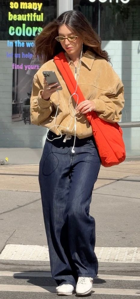 Tan suede jacket, wide-leg jeans, red shoulder bag, yellow sunglasses, and white sneakers.