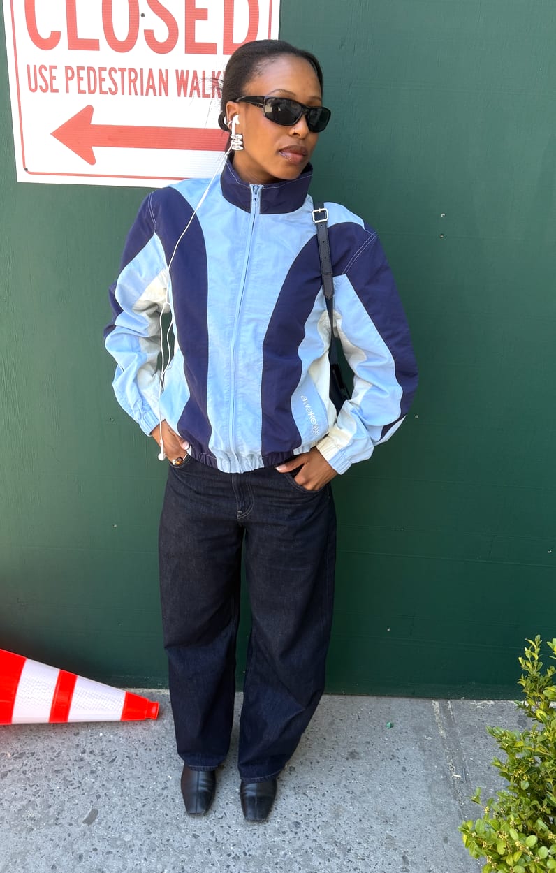 Navy and light blue color block windbreaker, dark wash jeans, black shoes, and sunglasses.