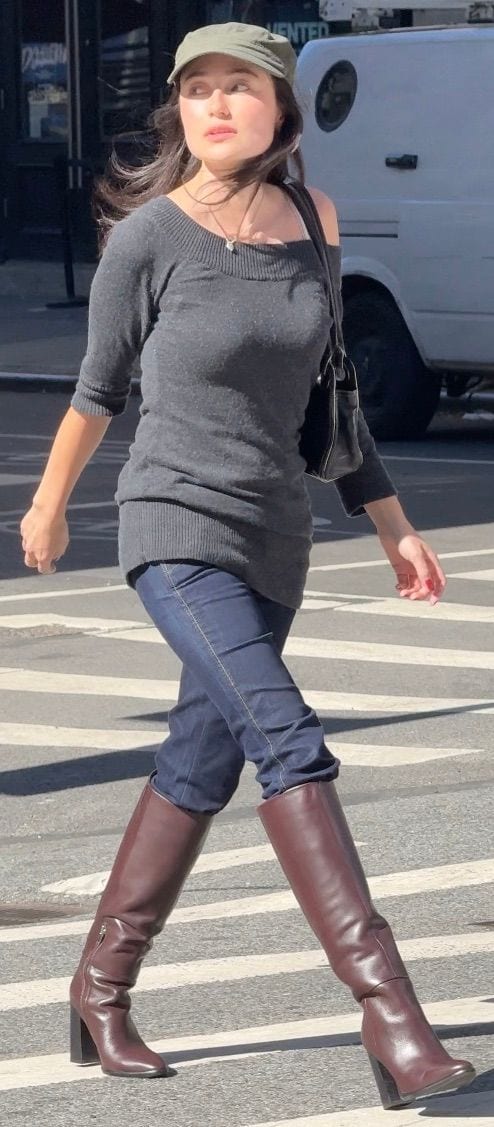 Gray off-shoulder sweater, blue jeans, and brown knee-high boots with an olive green cap.