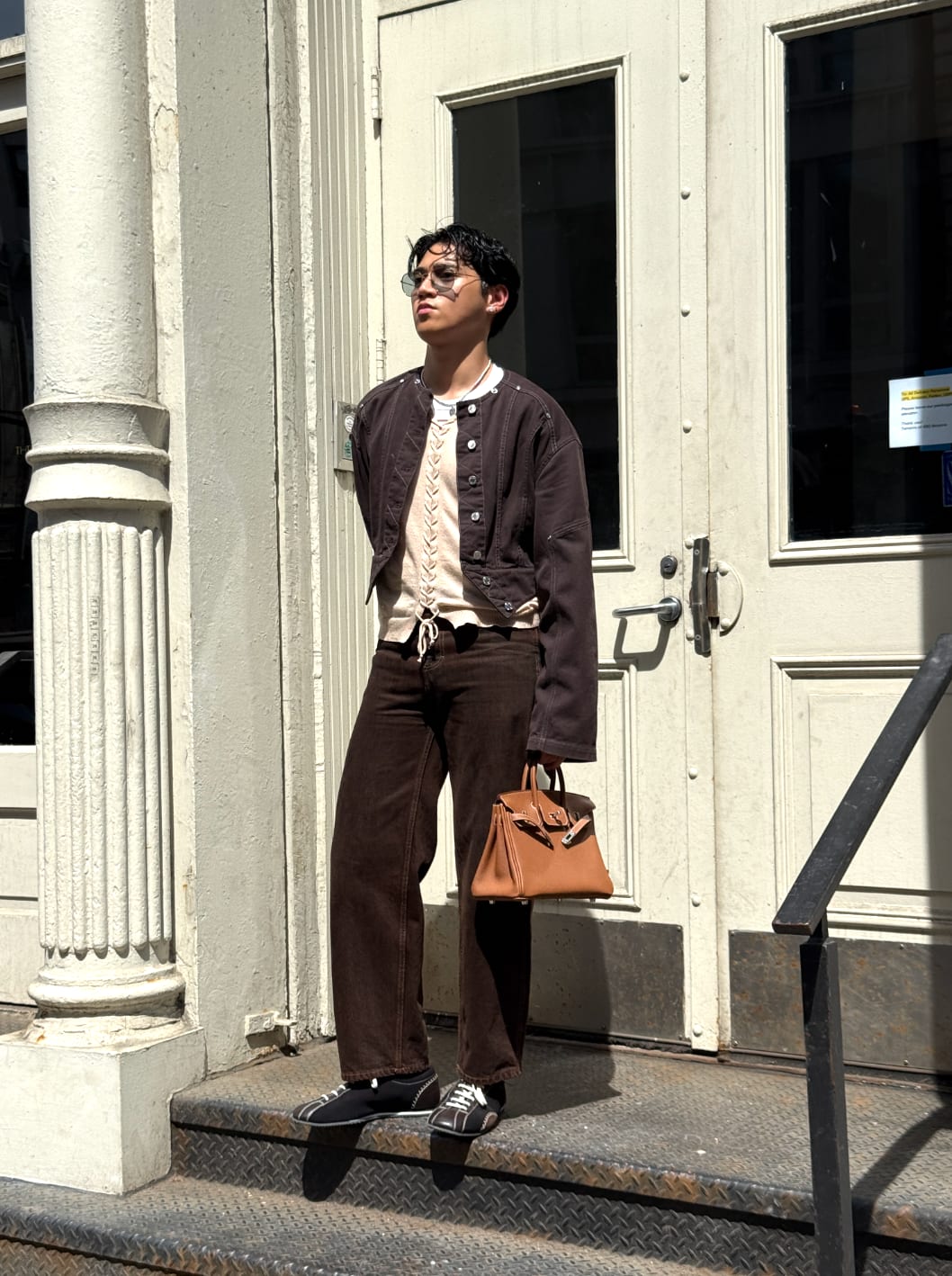 Brown jacket and pants, cream lace-up top, with tan Hermès Birkin bag.