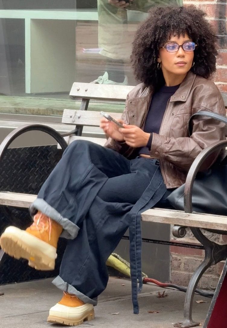 Brown leather jacket, black top, and wide-leg dark jeans with yellow lug sole boots.