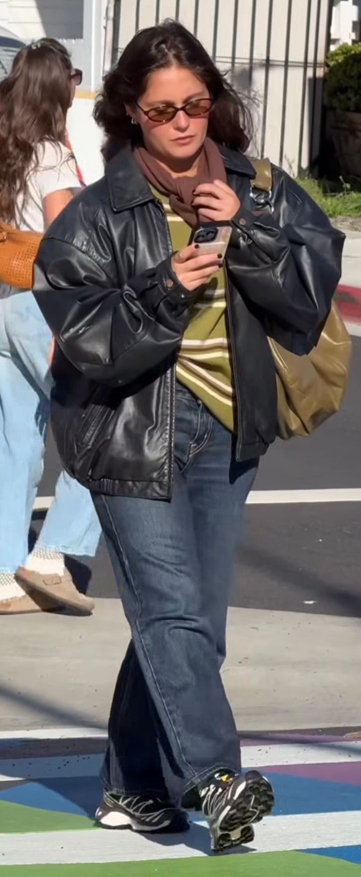 Black leather jacket, striped olive sweater, jeans, black sneakers, brown scarf and sunglasses.