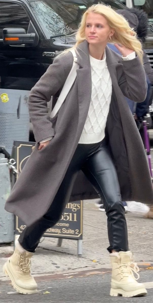 Gray long coat, white cable knit sweater, black leather leggings, and cream winter boots.