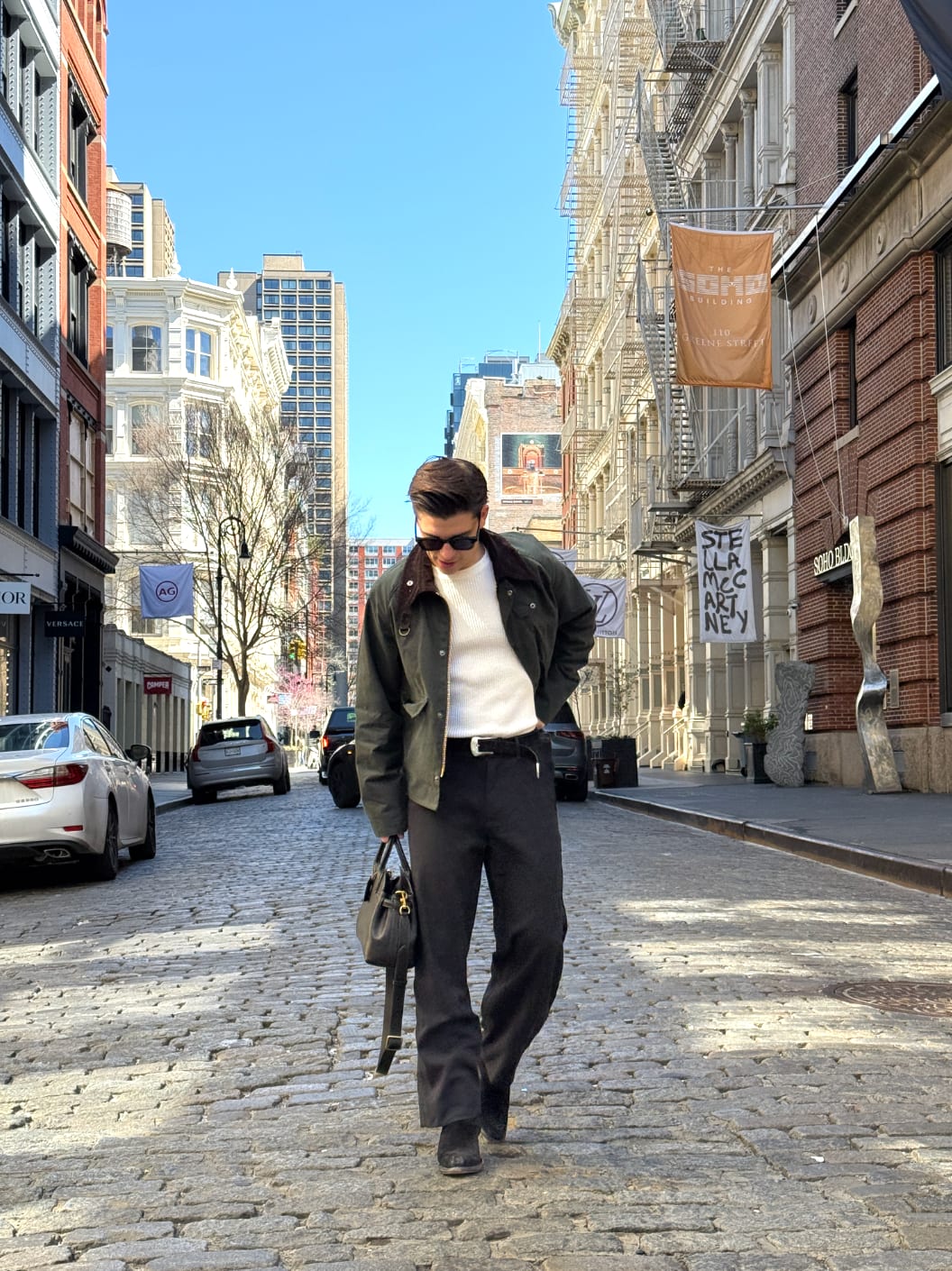 Green bomber jacket, white ribbed top, black pants, and black handbag on a cobblestone street.