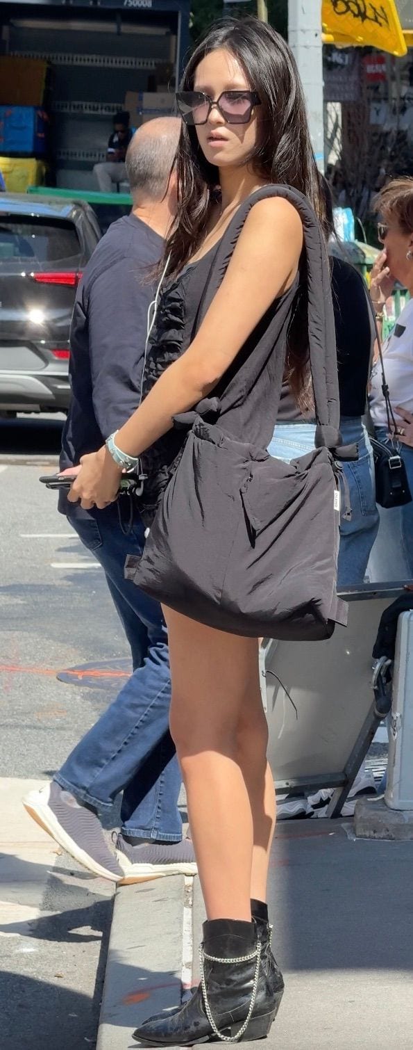 Black dress, sunglasses, and black chain boots, with a black shoulder bag on a city street.