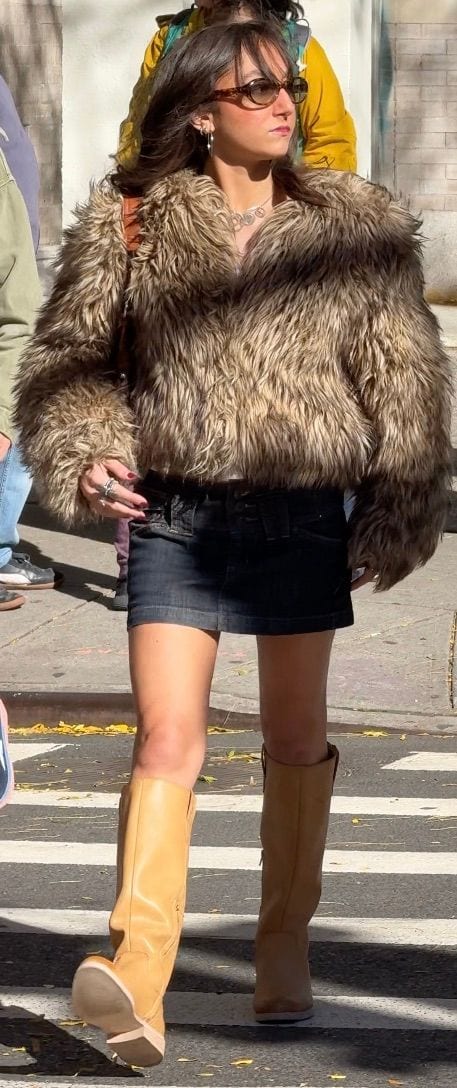 Faux fur jacket, dark denim mini skirt, knee-high tan boots, and sunglasses on a sunny street.