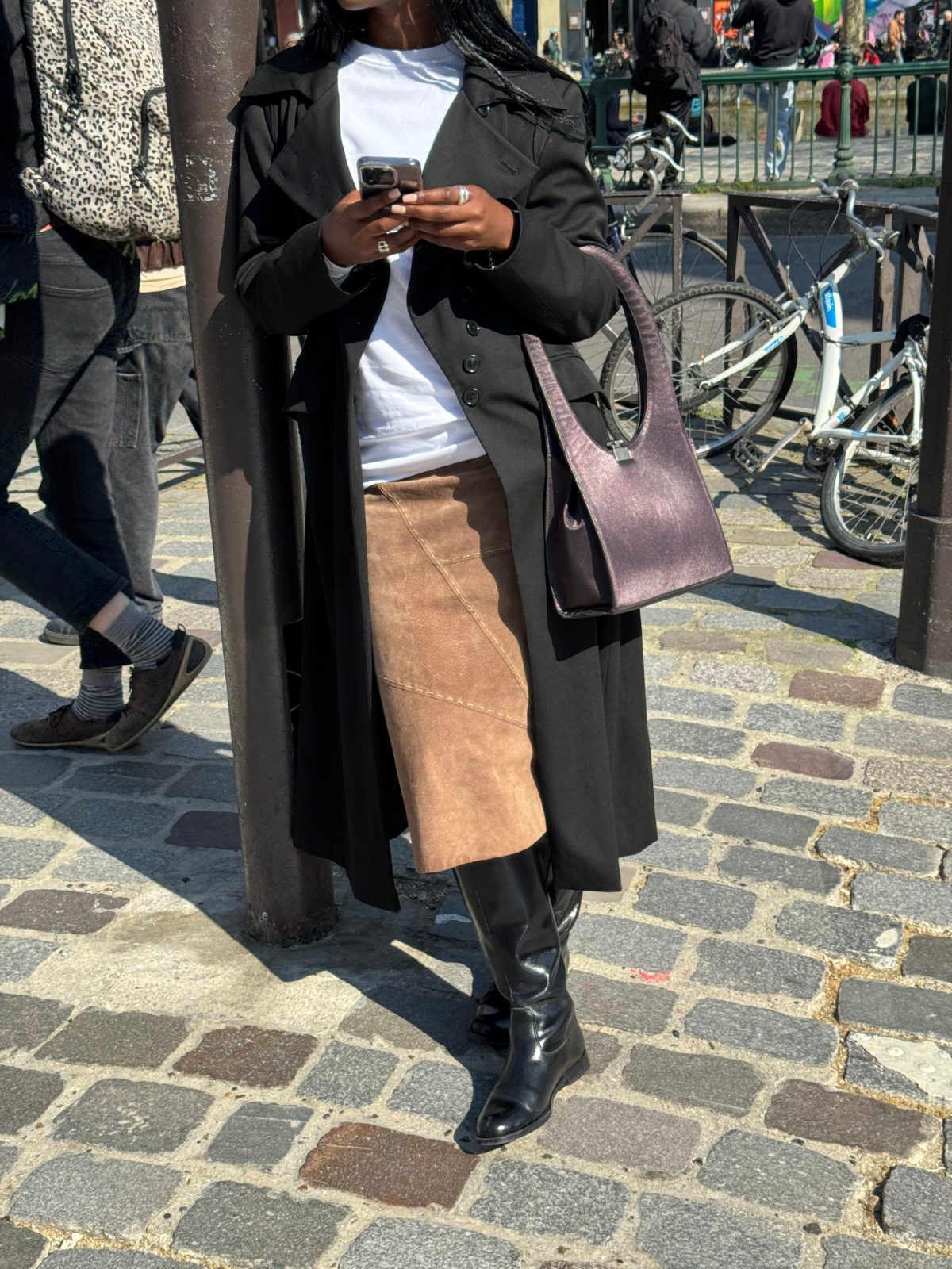 Black trench coat, white t-shirt, brown suede skirt, black boots, and a purple handbag.