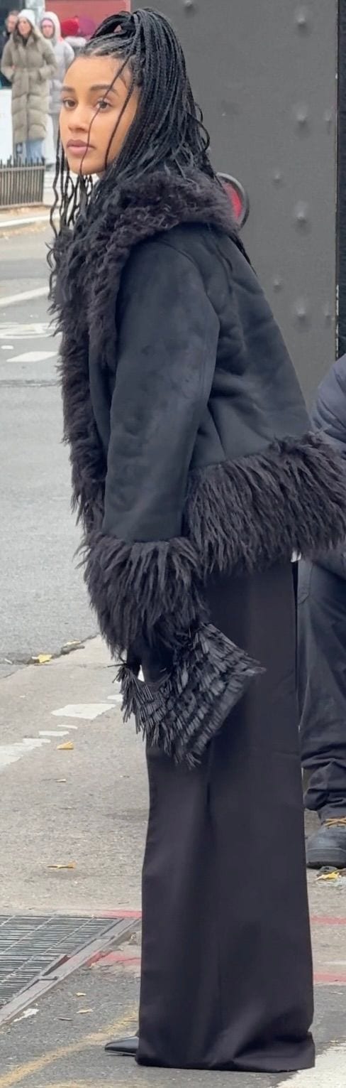 Black shearling-trimmed jacket, wide-leg pants, and feathered clutch. Braided hair.