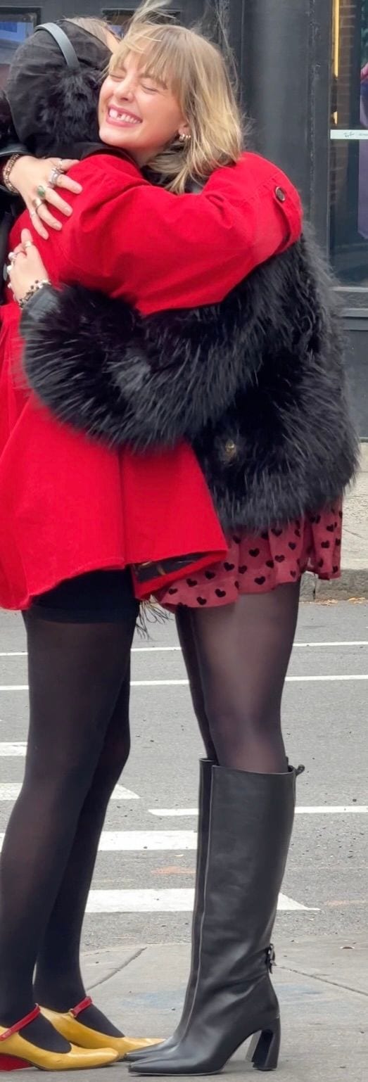 Red coat, black fur vest, heart print skirt, black tights, and black boots.