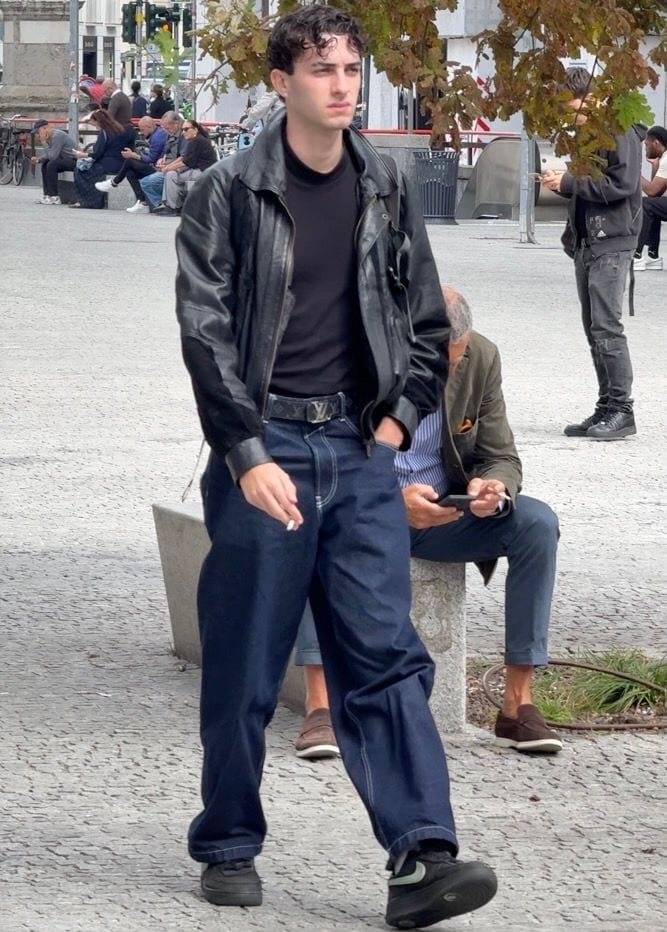 Black leather jacket, dark t-shirt, baggy denim jeans, black sneakers, and a LV belt.