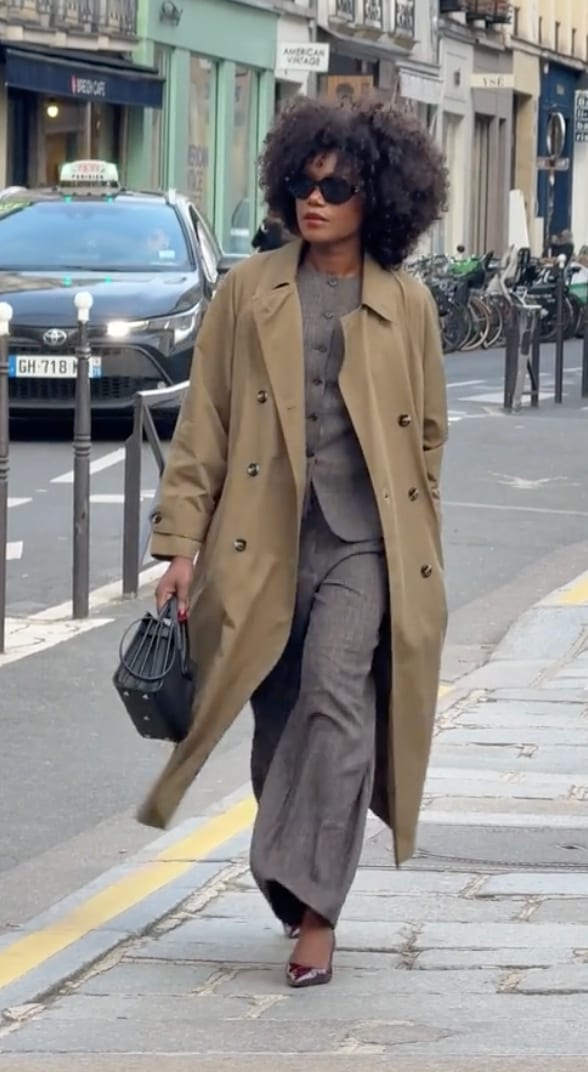 Tan trench coat over gray suit with wide-leg pants, black handbag, and red heels.