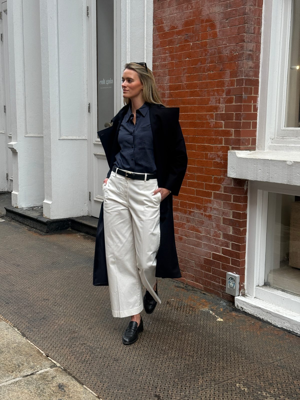 Navy collared shirt with a black coat, cream wide-leg pants, black belt, and black loafers.