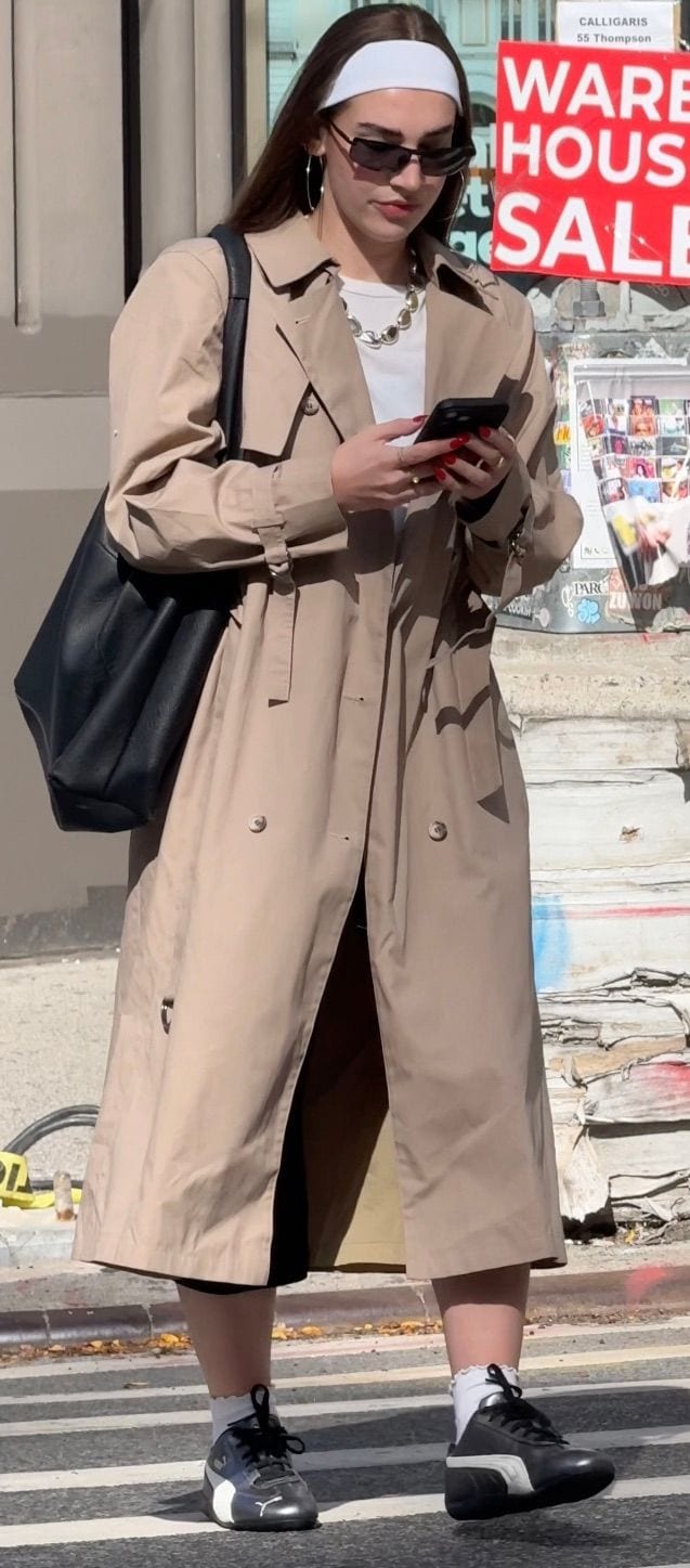 Beige trench coat with black sneakers, a white headband, and sunglasses.