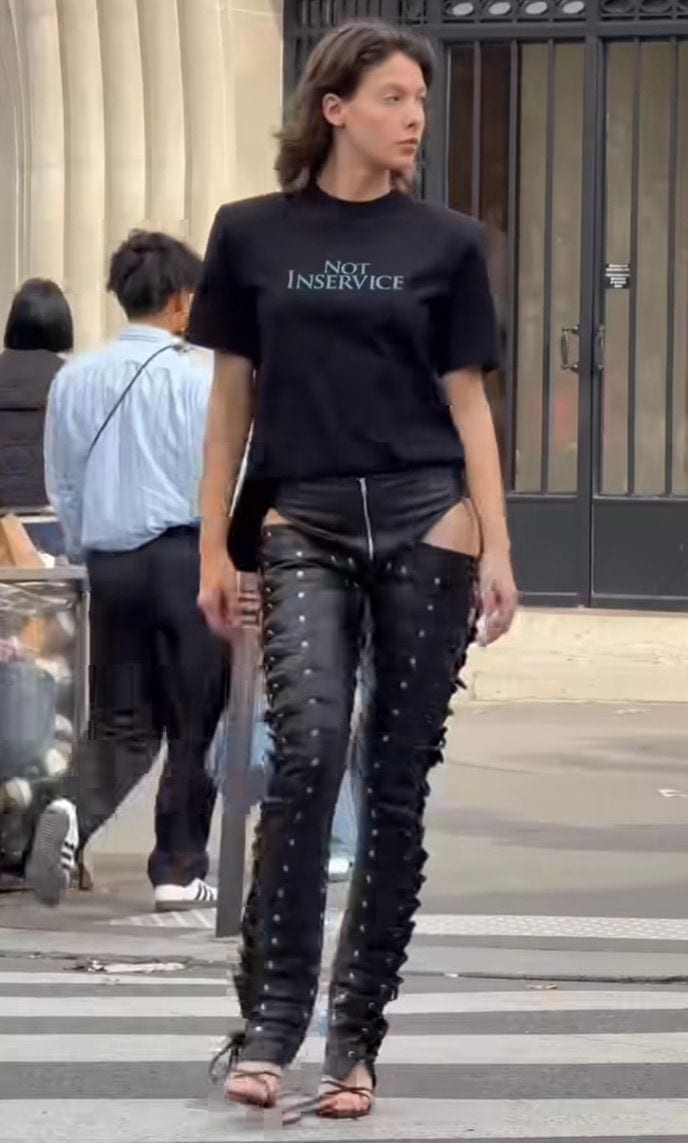 Black "NOT INSERVICE" tee with studded, lace-up leather chaps and strappy sandals.