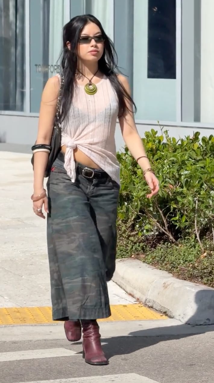 Pale pink knit top tied at waist, camo wide-leg pants, and burgundy boots.