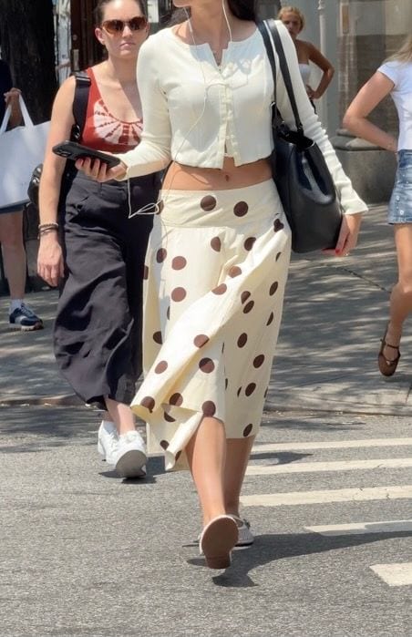 Cream cropped cardigan with a long polka dot skirt and black shoulder bag.