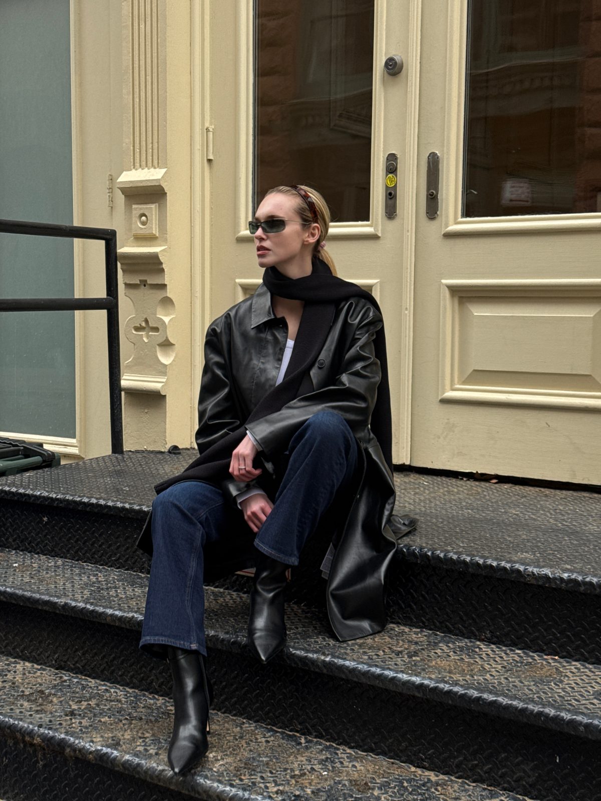 Black leather trench coat, denim jeans, black pointed-toe boots, scarf, and sunglasses.