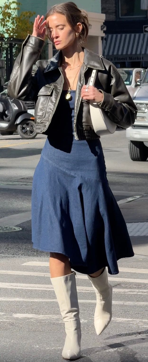 Brown leather bomber jacket, navy denim dress, white boots, and white shoulder bag.