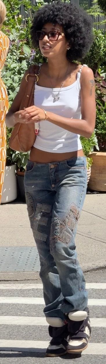 White tank top, patched denim jeans, brown sunglasses, and chunky sneakers.