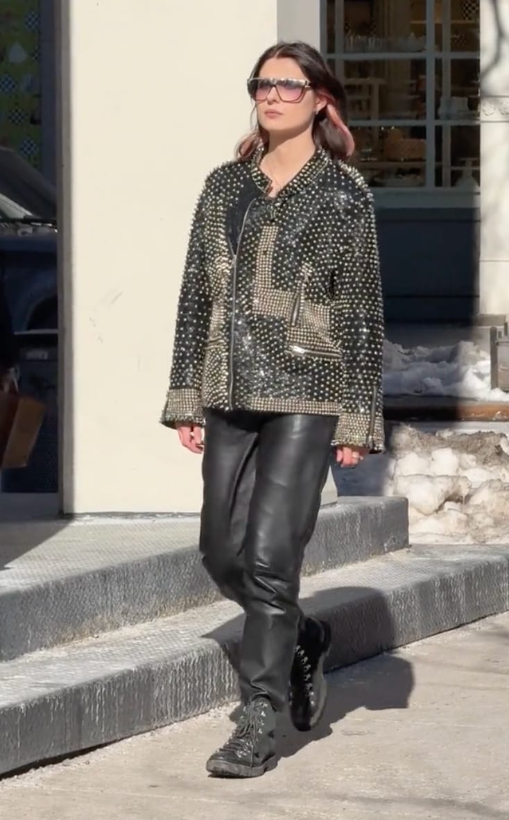 Black studded leather jacket, leather pants, and boots with pink sunglasses on a sunny street.