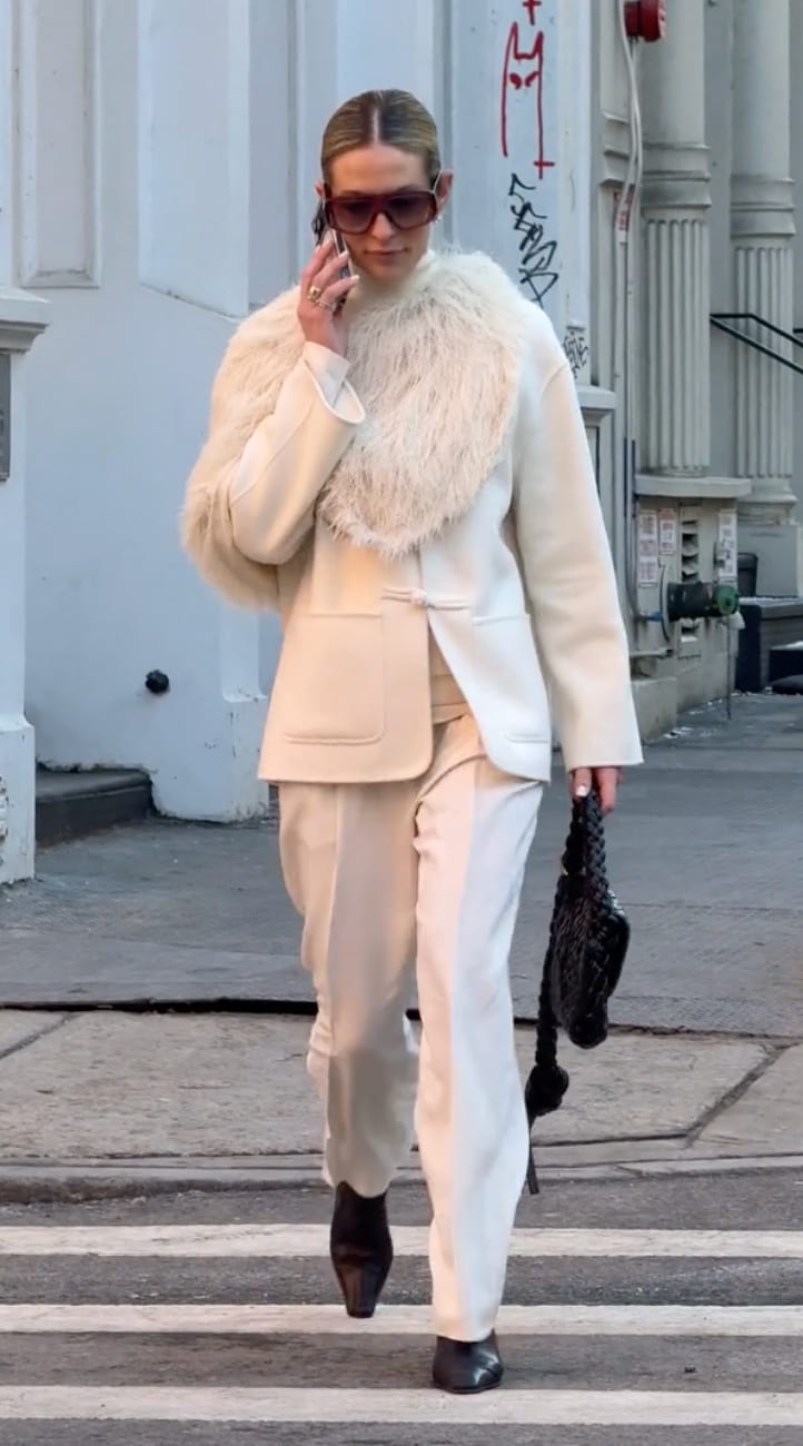 Cream wool coat with feathered collar, wide-leg trousers, sunglasses, and black braided bag.
