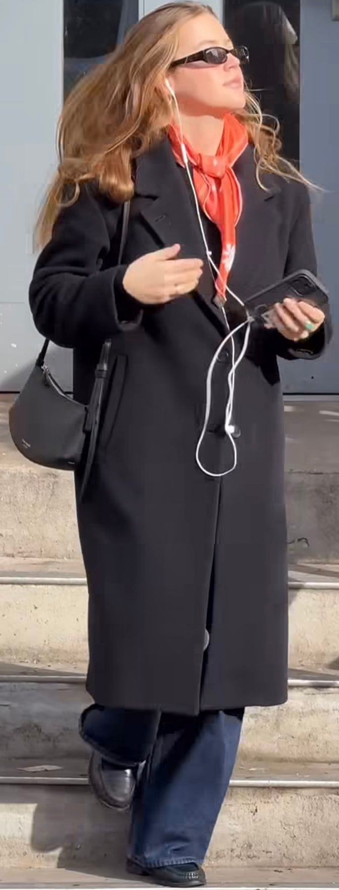 Black long coat, red neck scarf, dark sunglasses, black shoulder bag, blue jeans.