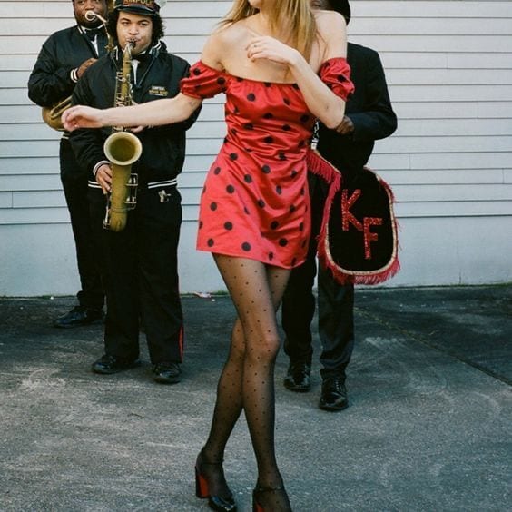 Red off-shoulder polka dot dress with sheer black stockings and musicians.