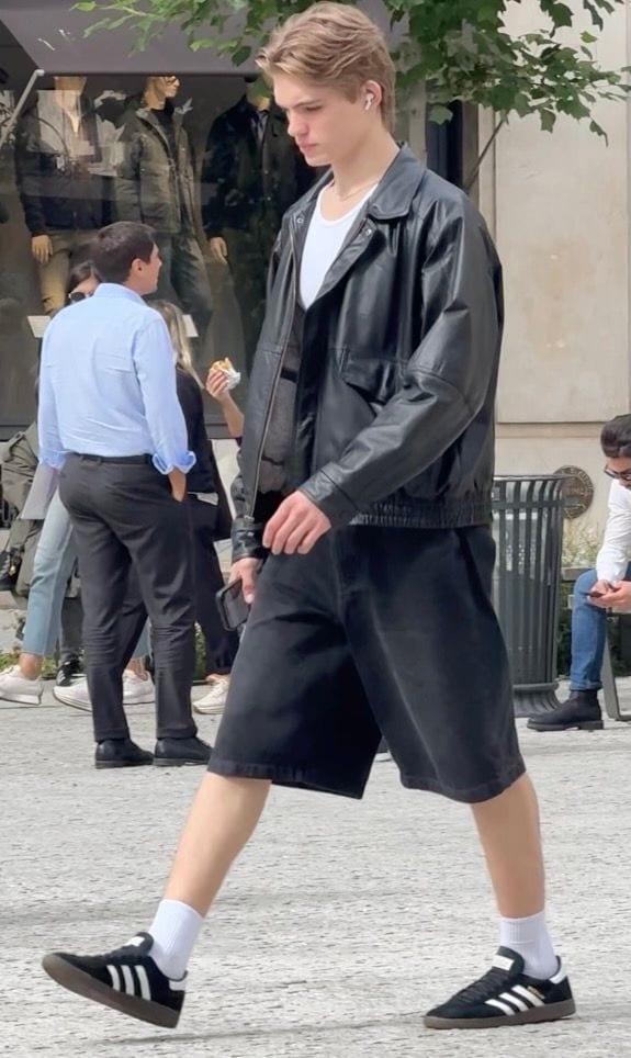 Black leather bomber jacket, white tee, long black shorts, and black Adidas sneakers.
