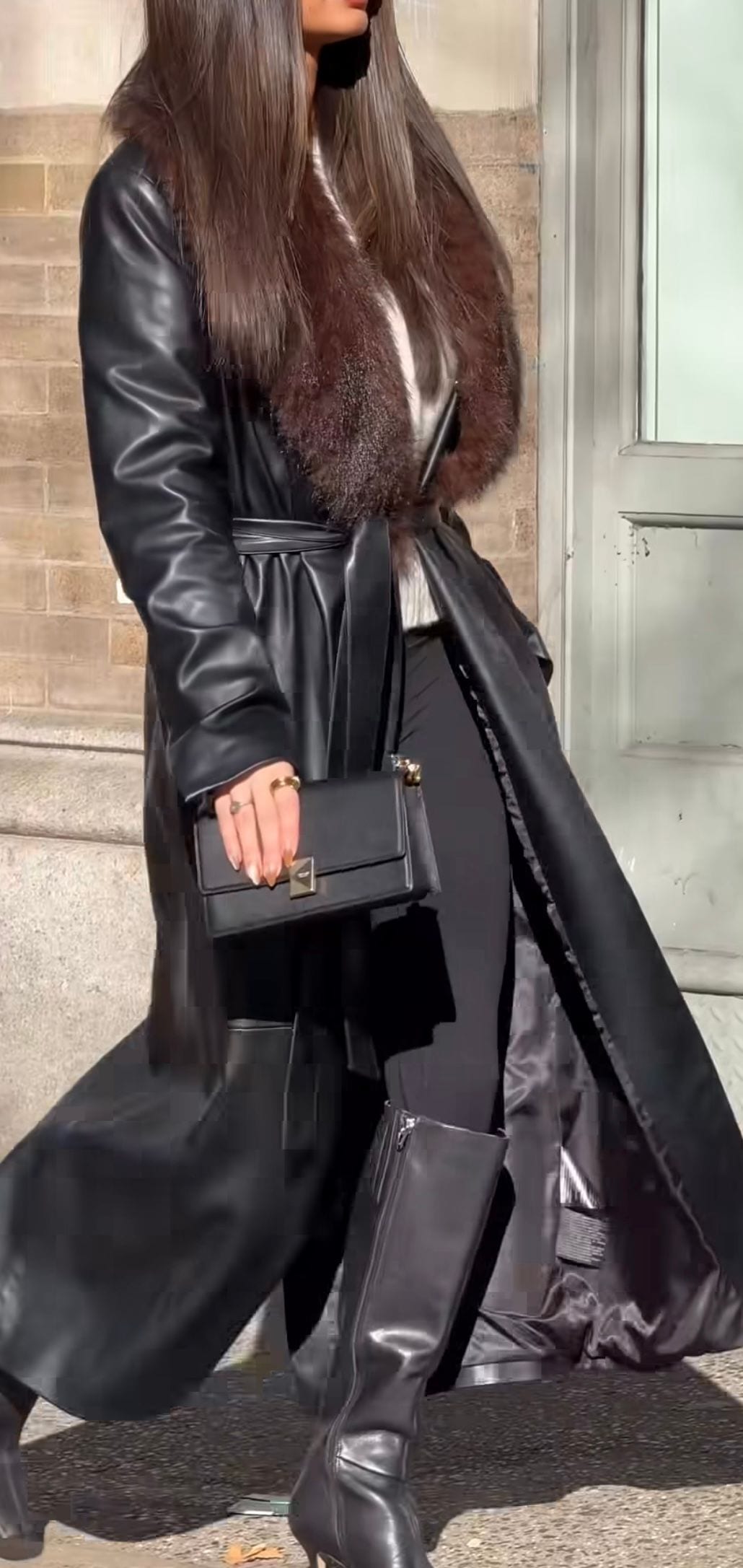 Black faux leather trench coat with brown fur collar, black knee-high boots, and black handbag.