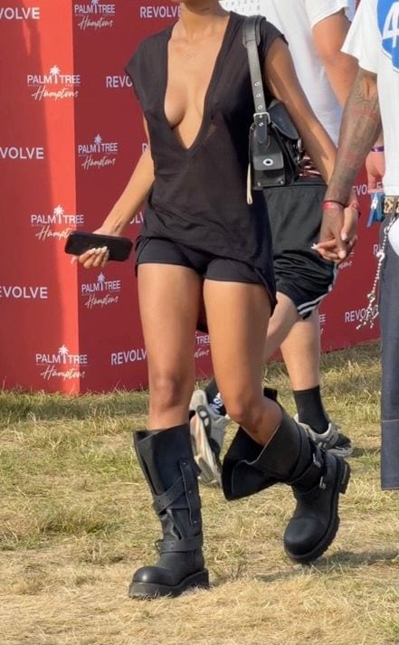 Black deep V-neck top, black shorts, and tall black combat boots with a shoulder bag.