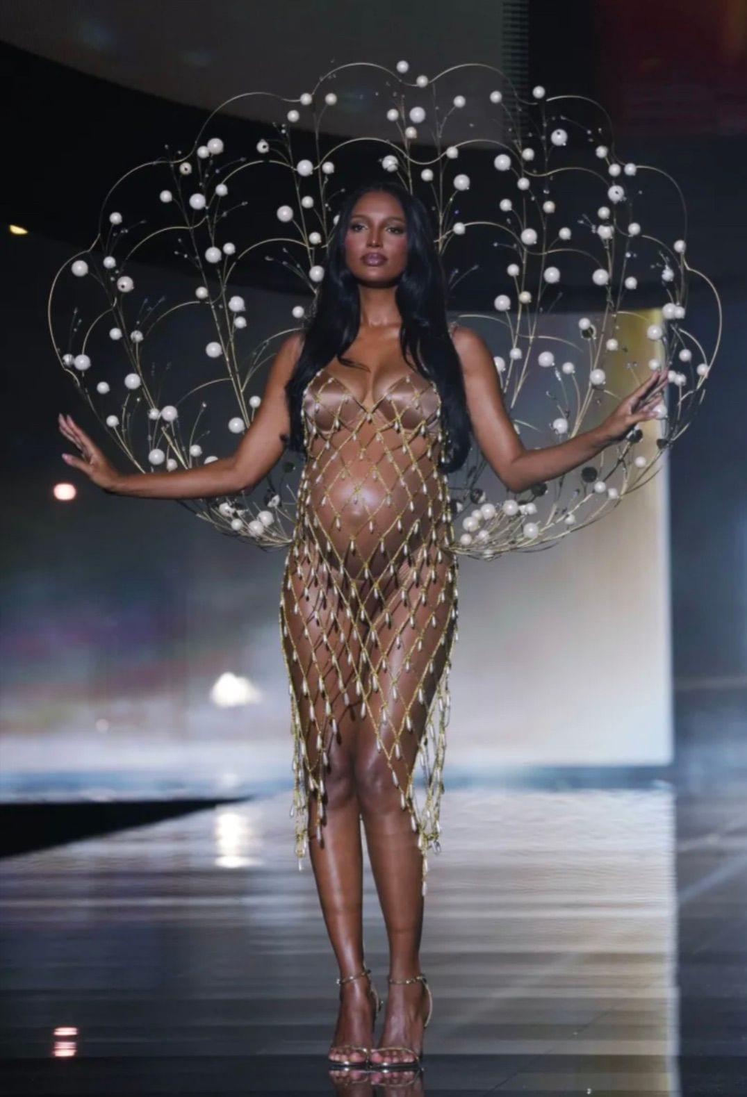 Pregnant model in sheer pearl-embellished gown with elaborate pearl wings and gold heels.