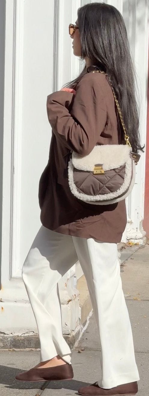 Brown blazer with white wide-leg pants, brown shoes, and a shearling trim quilted bag.
