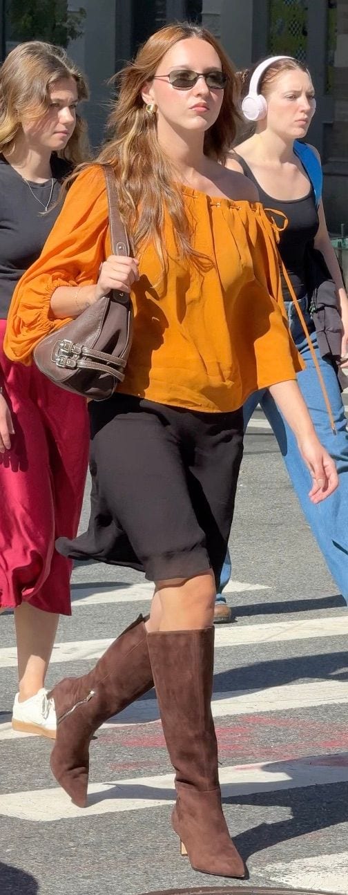 Orange off-shoulder top, black midi skirt, brown suede boots, and dark sunglasses.