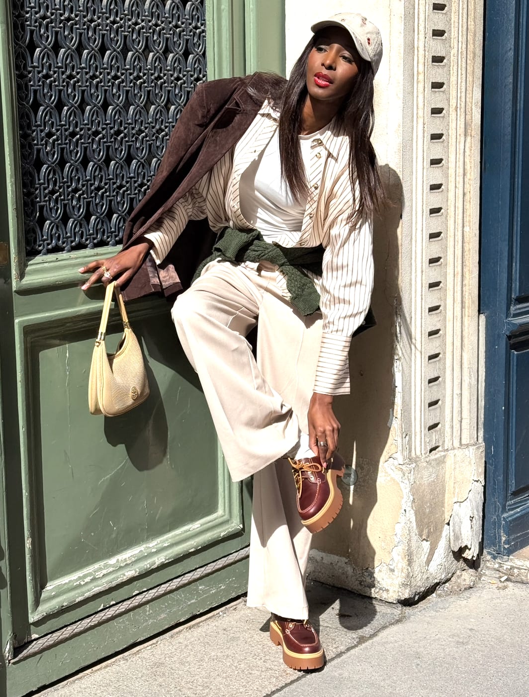 Brown suede jacket over striped shirt, beige pants, green sweater, and platform loafers.
