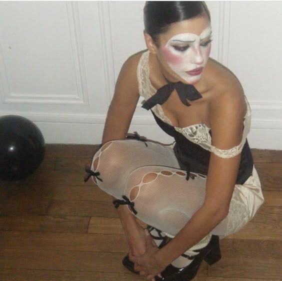 Mime in black corset, lace top, fishnet tights with bows, and patent Mary Janes.