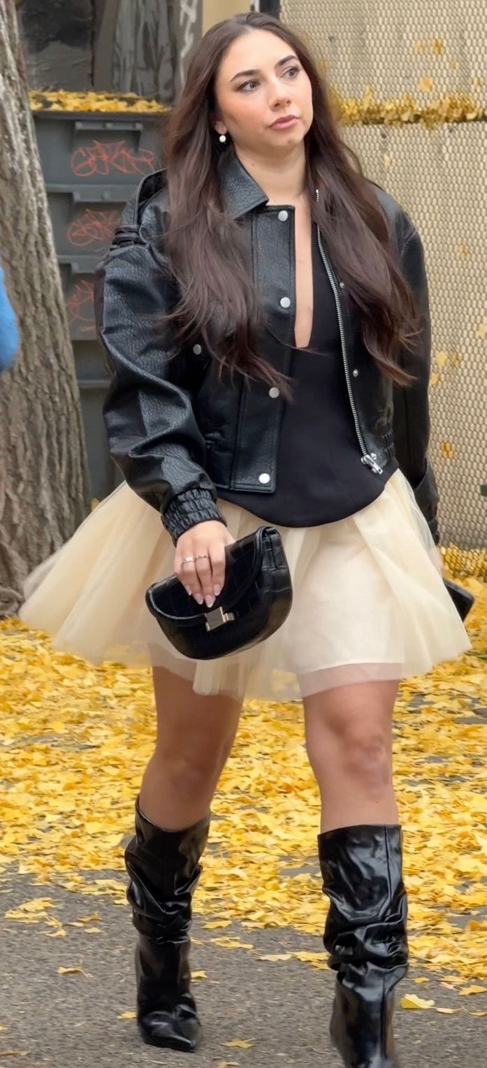 Black leather jacket, tulle skirt, black boots, and matching handbag on yellow leaves.