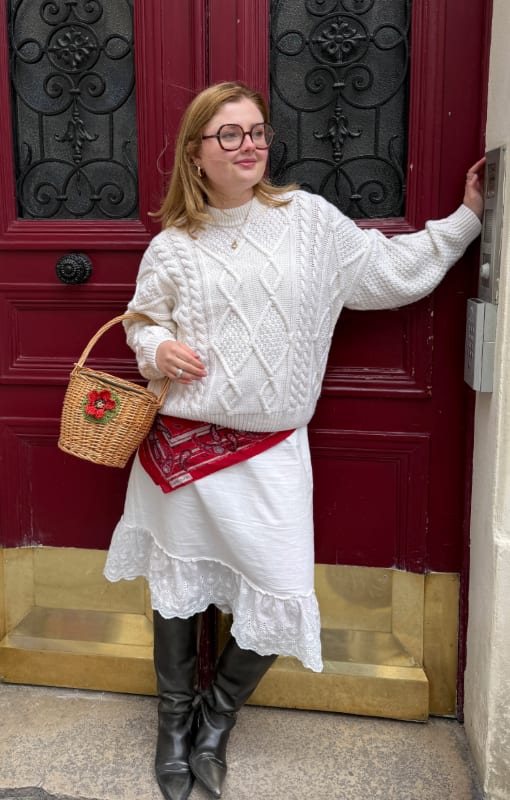White cable knit sweater, lace trim skirt, black boots, red bandana, and a wicker basket.