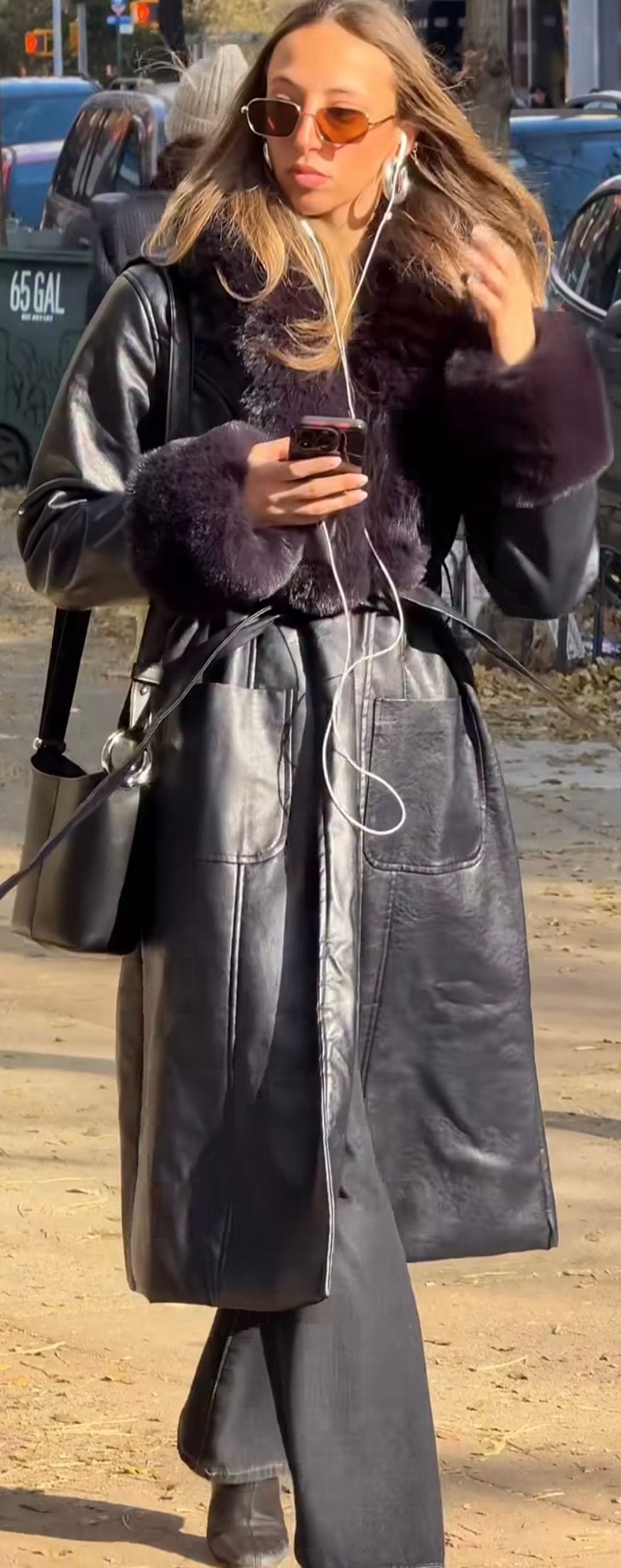 Black leather trench coat with faux fur trim, wide-leg pants, and amber sunglasses.
