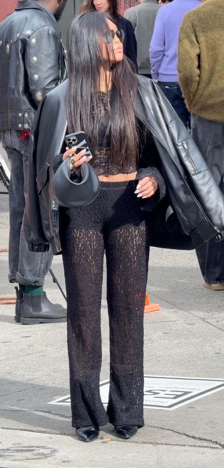 Black lace cropped top and sheer pants, leather jacket, sunglasses, and black bag.