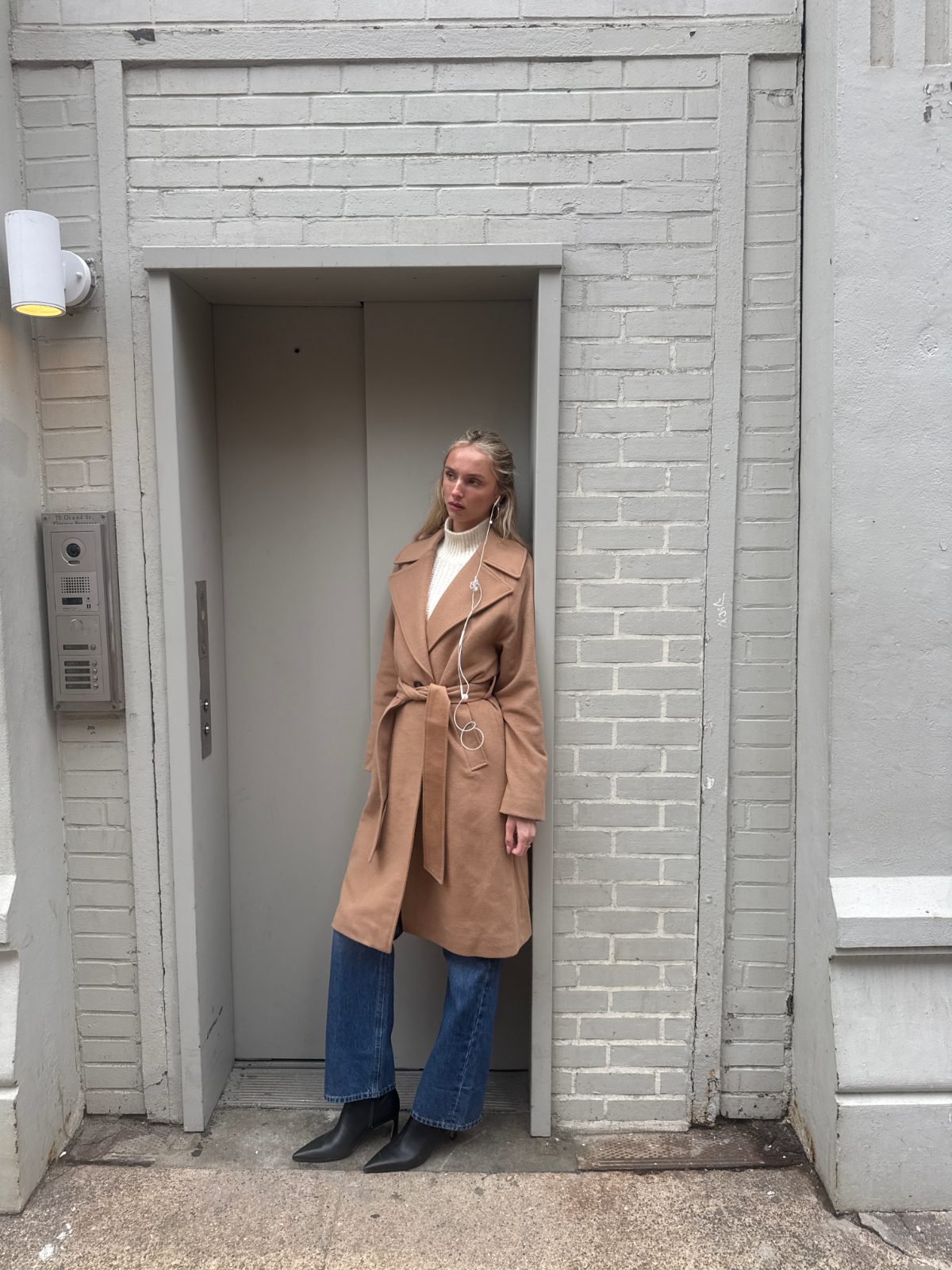 Camel wool coat with a white turtleneck, blue jeans, and black ankle boots.