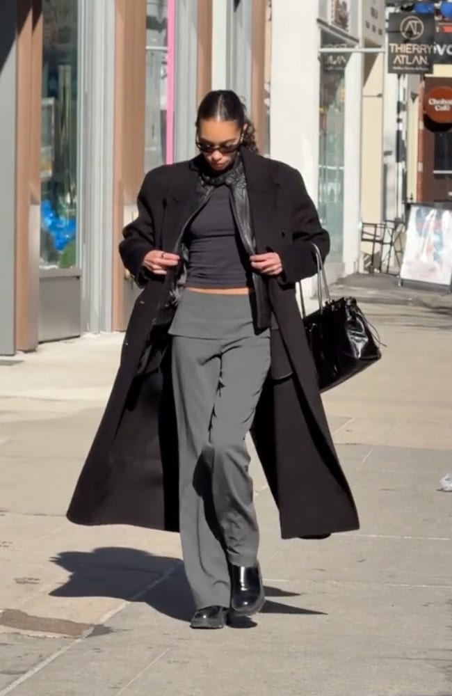 Black oversized long coat, gray trousers, black top, and black leather bag on a sunny street.