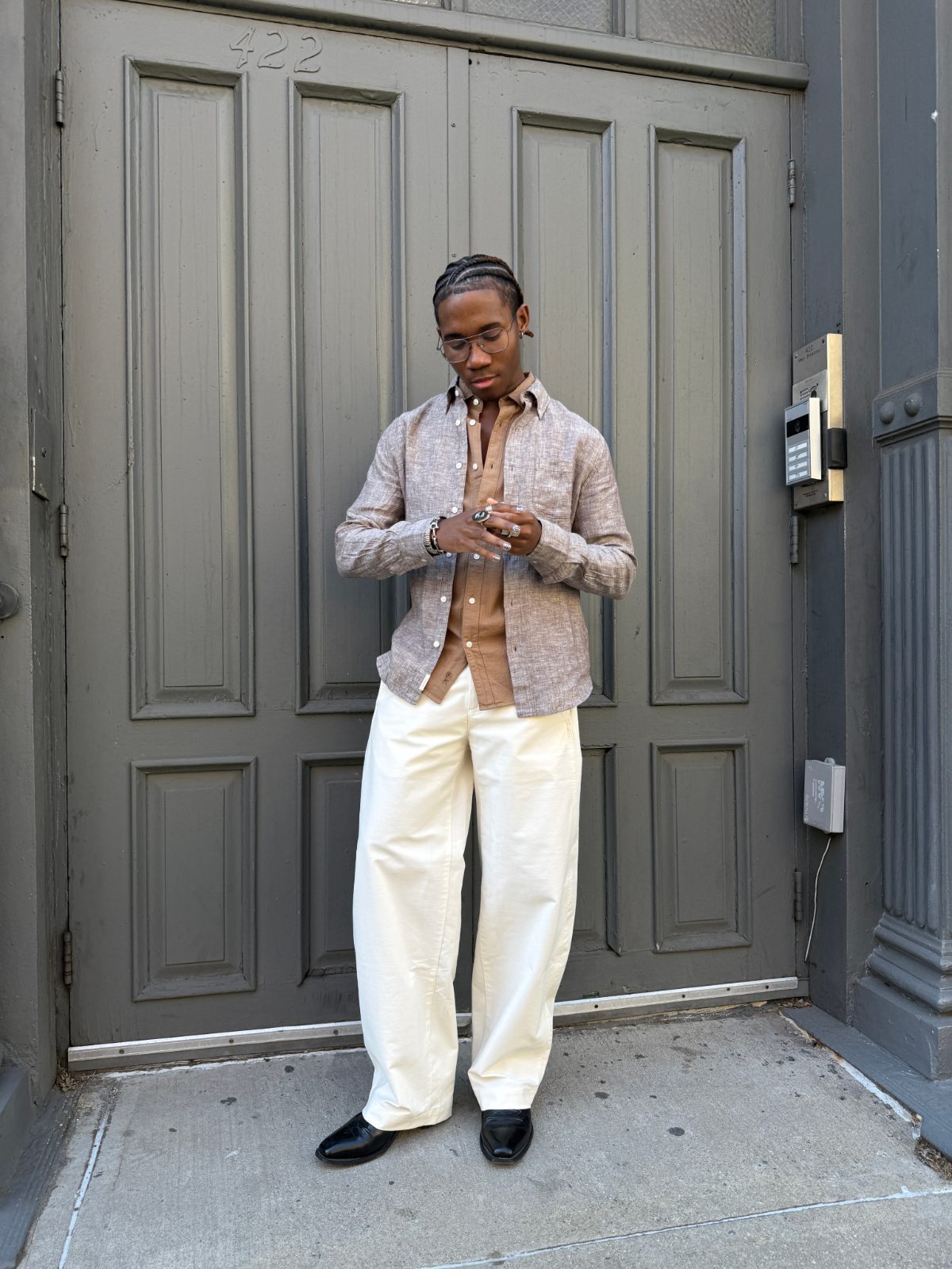 Light brown linen shirt over a darker brown shirt, cream wide-leg pants, black dress shoes.
