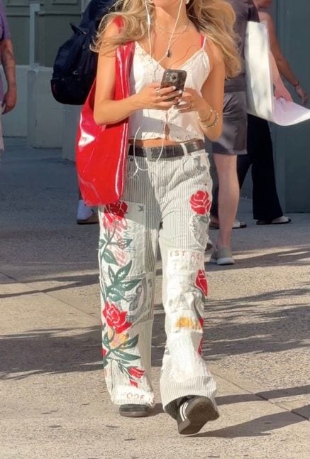 White lace camisole, striped pants with red rose patches, black belt, and red shoulder bag.