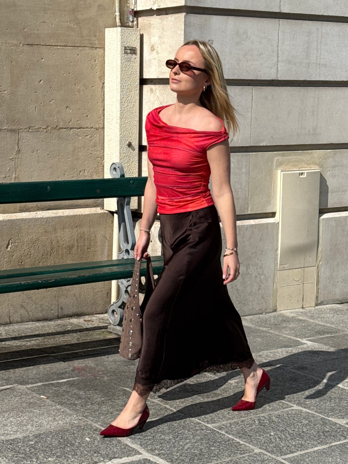 Red off-the-shoulder top, brown lace-trim skirt, and red heels on a sunny street.