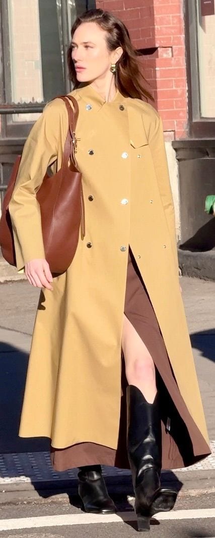 Tan double-breasted trench coat with golden buttons, brown slip dress, black boots, brown tote bag.