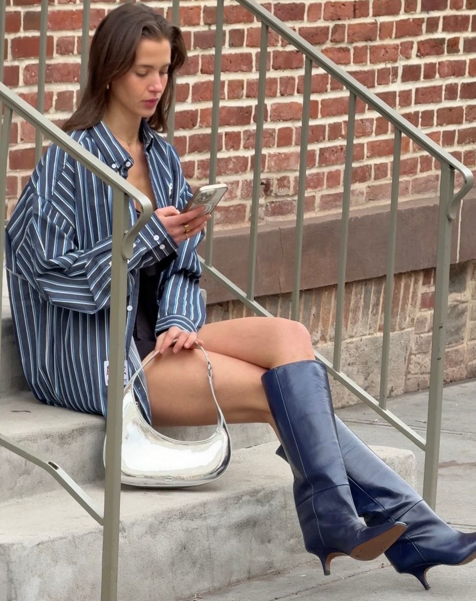 Blue striped oversized shirt, black shorts, silver crescent bag, and navy knee-high boots.