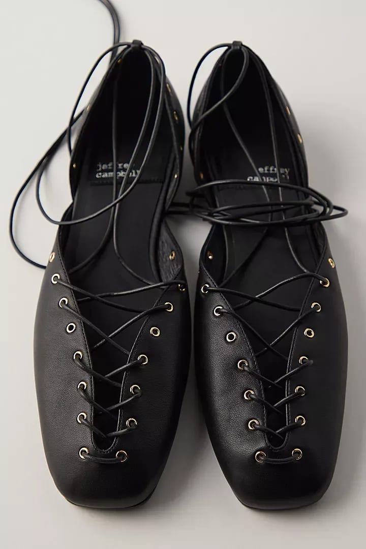 Black leather lace-up ballet flats with gold eyelets and ankle ties.