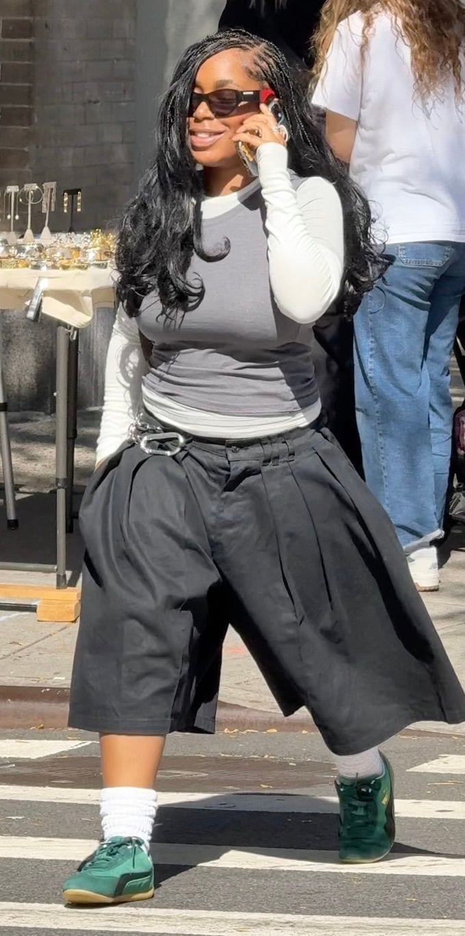 Gray tank top over white long-sleeve, black pleated culottes, green sneakers.