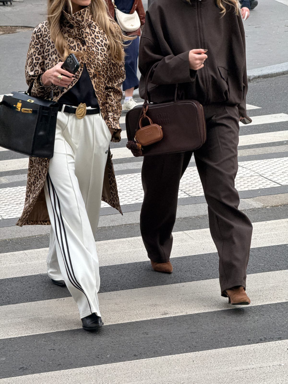 Leopard print coat, white track pants, and a black bag next to a person in a brown tracksuit.