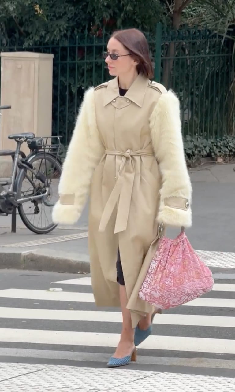 Tan trench coat with cream faux fur sleeves, blue mules, and a pink patterned bag.